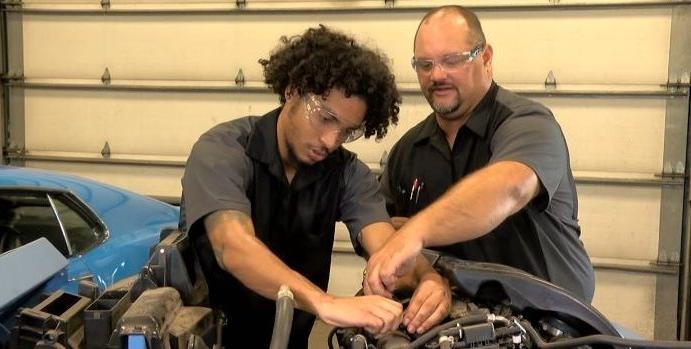 指导老师帮助学生修理汽车发动机